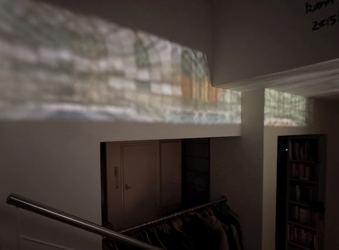 Oberlicht-Band. Auf der gegenüberliegenden Wand erscheinen die vergrößerten und verzerrten Bleiverglasungen als bunte Lichtschatten.